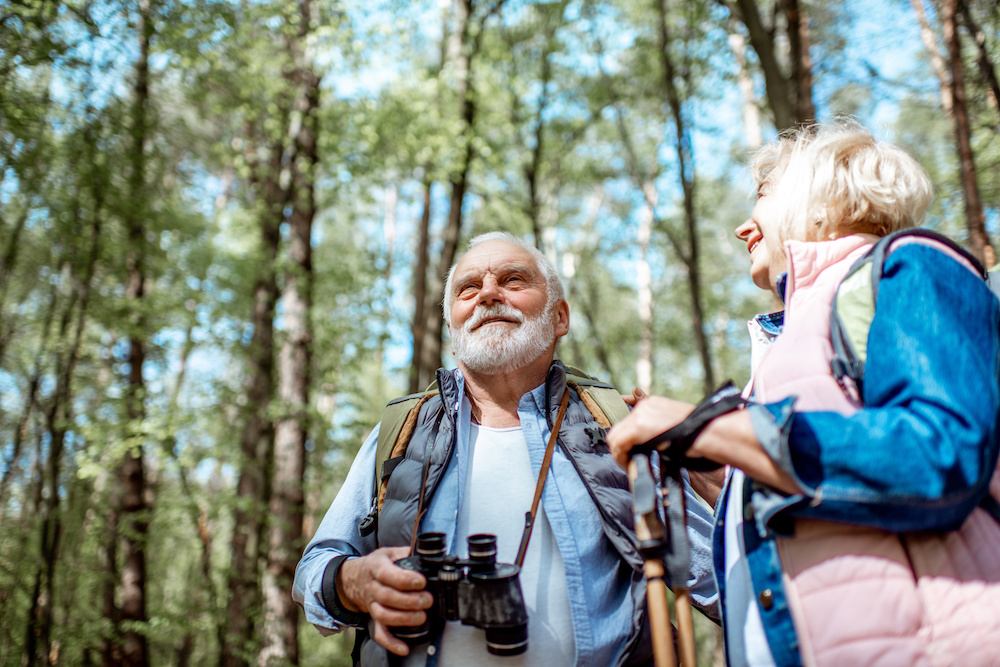 Senior couple looking with binoculars while hiking in the forest. Concept of an active lifestyle on retirement