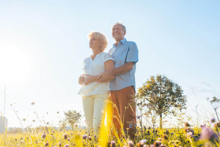 Low-angle view of a romantic elderly couple enjoying health and nature while standing together on a field in a sunny day of summer